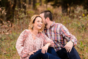 middle georgia engagement session couple in pink and blue jeans sitting in field laughing and holding each other