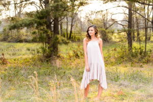 middle georgia senior portrait session, brown haired girl standing in field at sunset