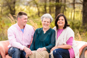 grandmother in green shirt sitting on sofa in field with daughter in pink and white shirt and grandson in pink shirt portrait session