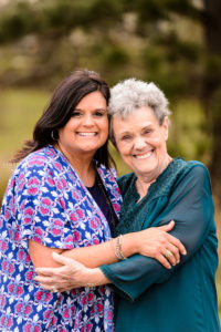 grandmother in green shirt hugging daughter in blue and pink shirt in field in middle georgia during portrait family photosession