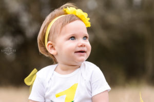 little blonde girl standing in field in yellow tutu and yellow flowered headband