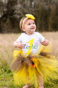 little girl in field smiling wearing a yellow tutu and flowered headband