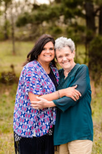 grandmother in green shirt hugging daughter in blue and pink shirt in field in middle georgia during portrait family photosession