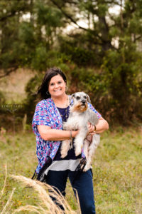 lady in blue and pink shirt holding her puppy in field for portrait session middle georgia